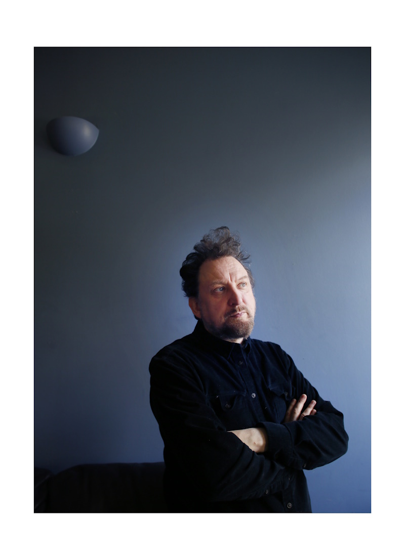 author ewan morrison looks pensively upwards, likel;y he can see the truth, he wears dark clothes and his hair stands up proudly and artistically above him 